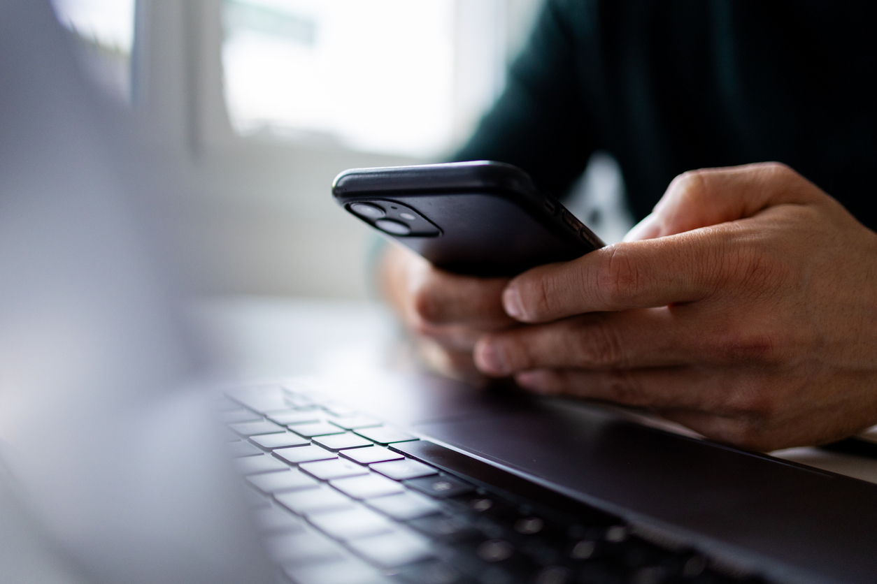 A person holding a smartphone with a laptop keyboard in the foreground.