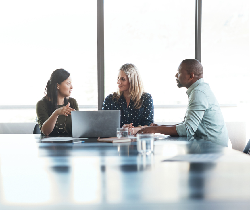 Image of three people in a business meeting, looking over a laptop
